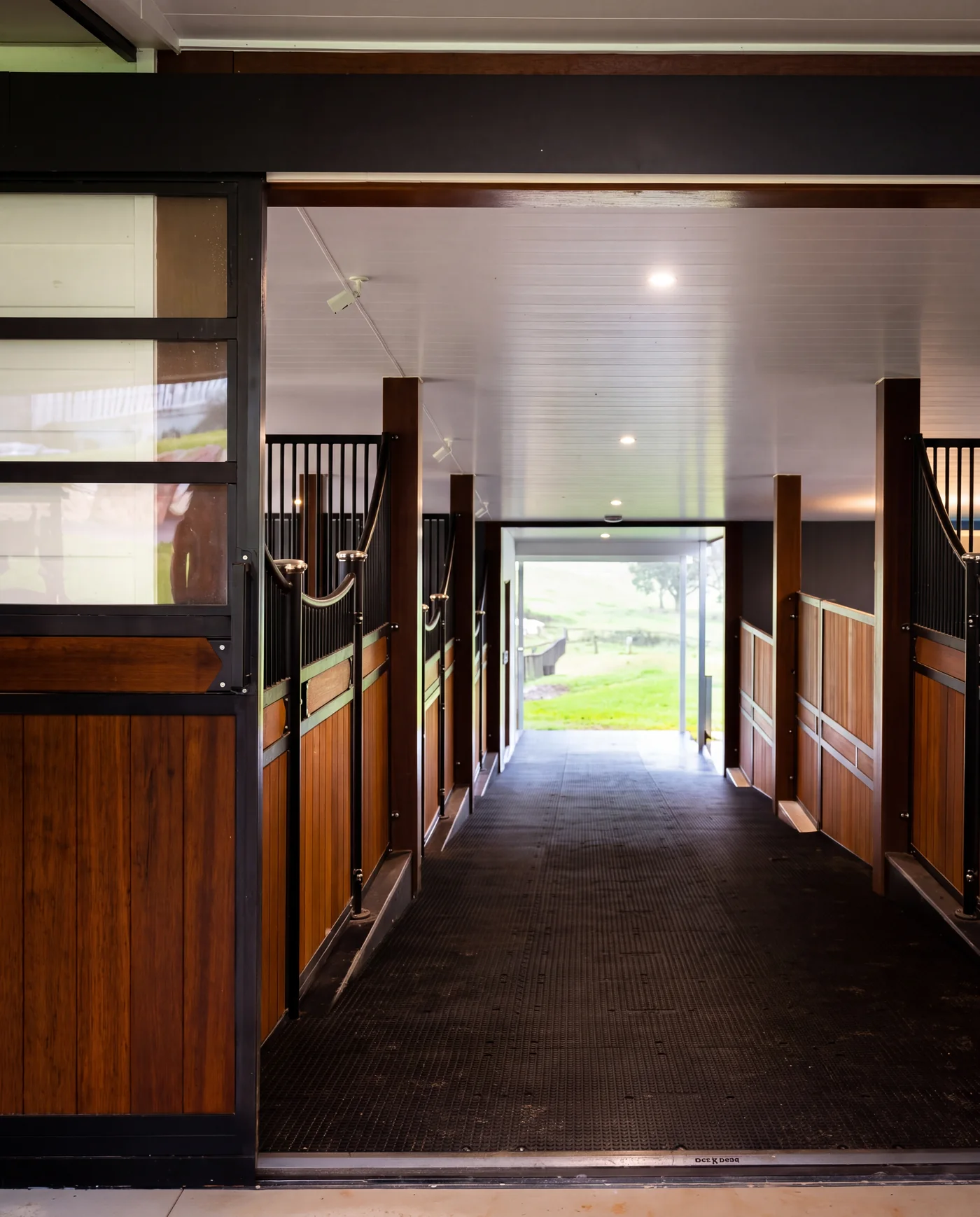 Stable aisle with timber and black steel fronts opening onto paddocks