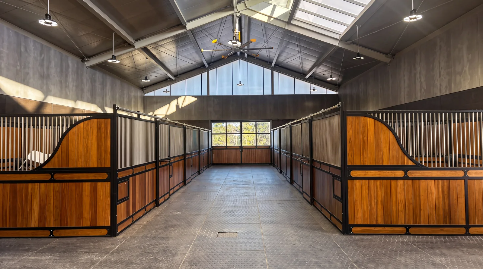 A stable aisle lined with curved timber and black steel stable fronts